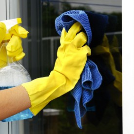 woman polishing glass door using microfiber cloth and yellow latex gloves